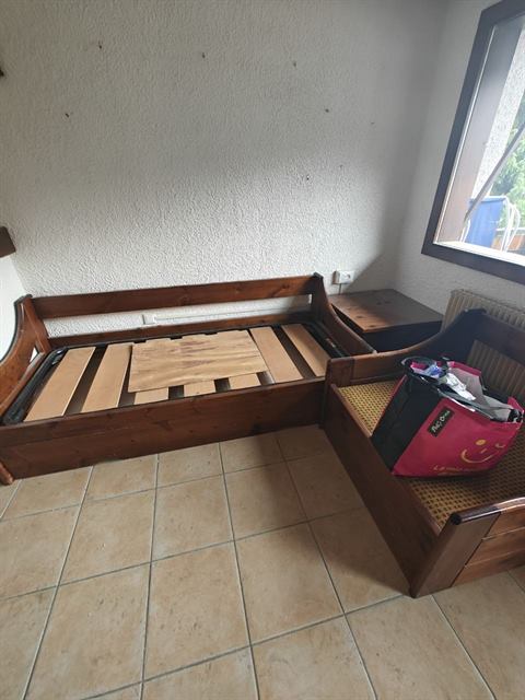 Due divani letto in legno con le doghe scoperte e una borsa appoggiata, prima della pulizia