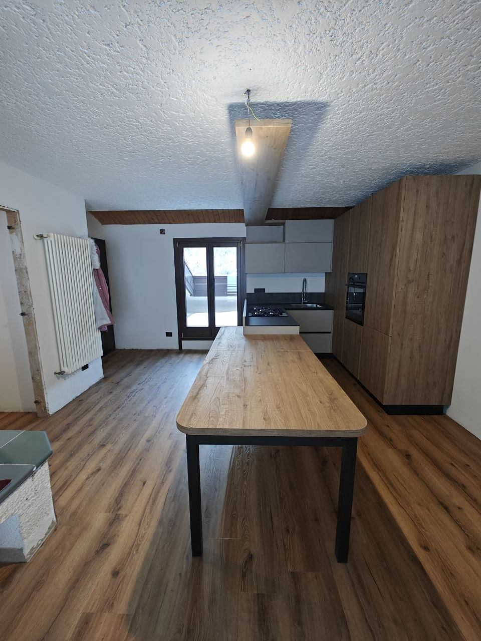 La stessa cucina open space sgombra e pulita, con pavimento in legno libero e tavolo in ordine