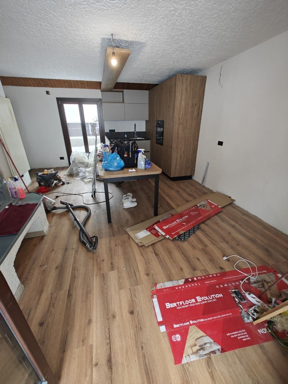 Cucina open space a fine lavori, con scatoloni del pavimento, attrezzi e sacchi sparsi a terra